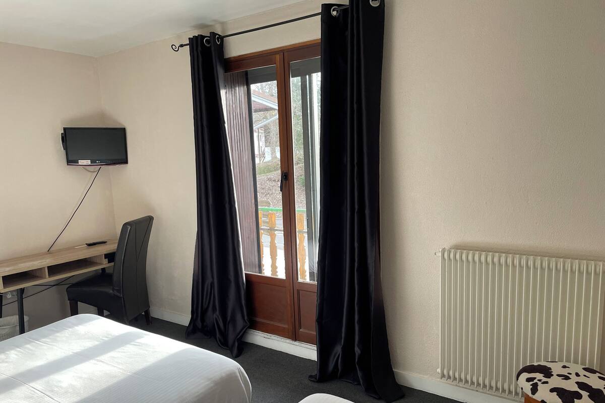 A hotel room with two beds, a desk with a chair, a television, and a window with curtains.