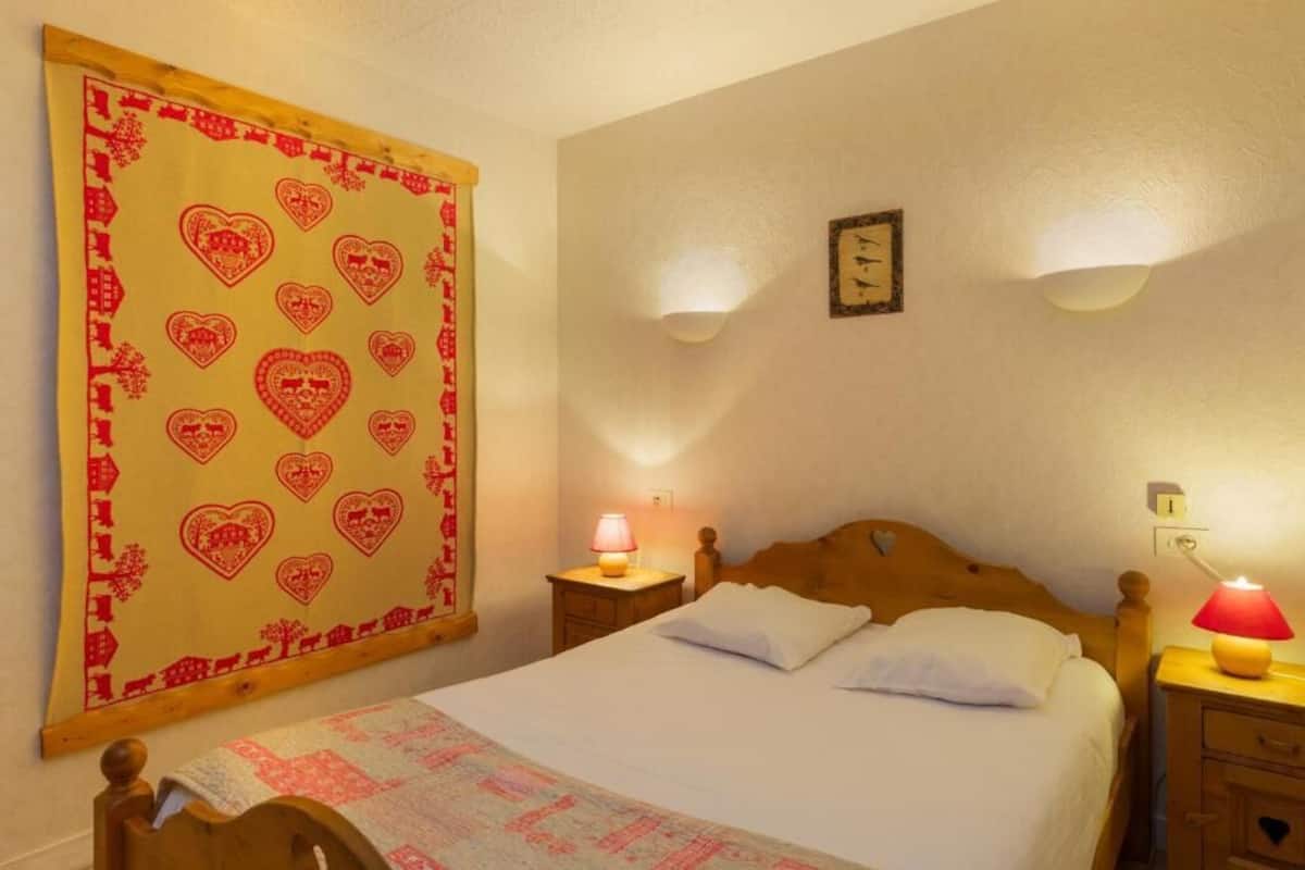 A bedroom with a bed, two bedside tables, a wall clock, and a large heart-patterned tapestry.