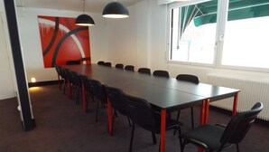 Un salón de conferencias con una larga mesa, sillas negras e iluminación colgante.