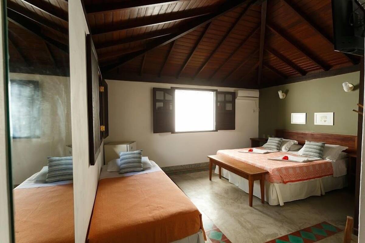 A room with two beds, a wooden ceiling, a window, and a wall-mounted TV.