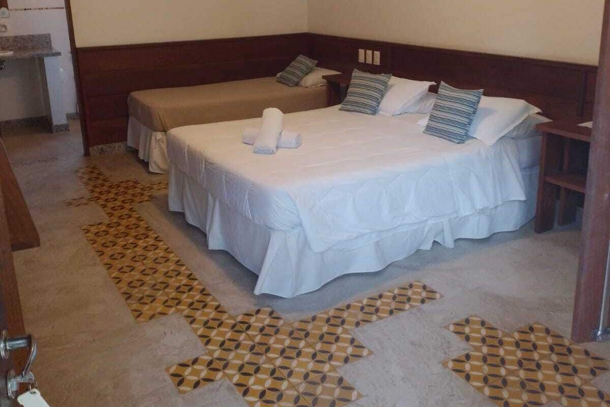 A hotel room with a bed, a bench, a small table, and a wall-mounted light.