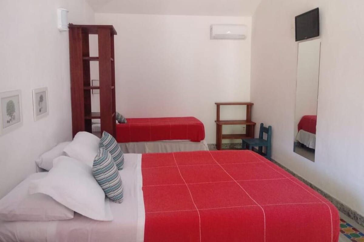 A bedroom with a bed, a red blanket, a wooden ladder, a small table, and a mirror on the wall.