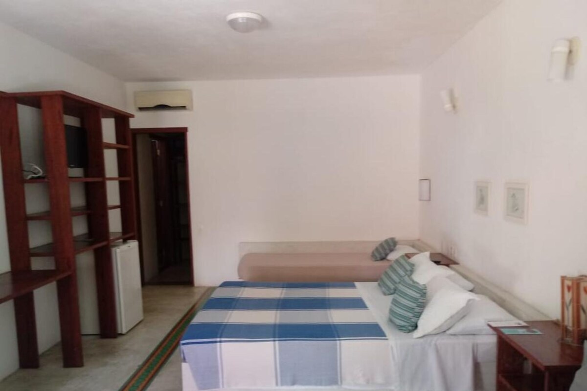 A bedroom with a bed, a wooden wardrobe, a small table, and a door leading to another room.