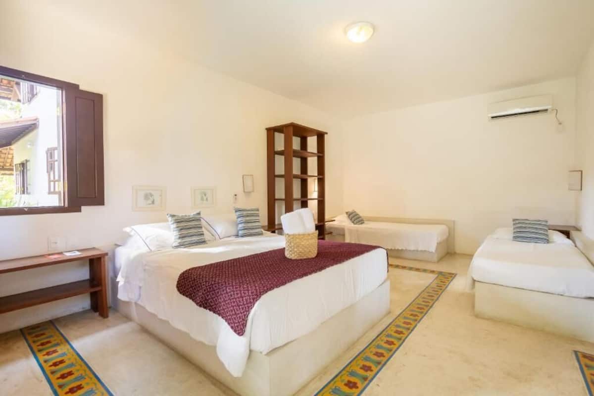 A hotel room with two beds, a wooden shelf, a window, and a patterned rug.