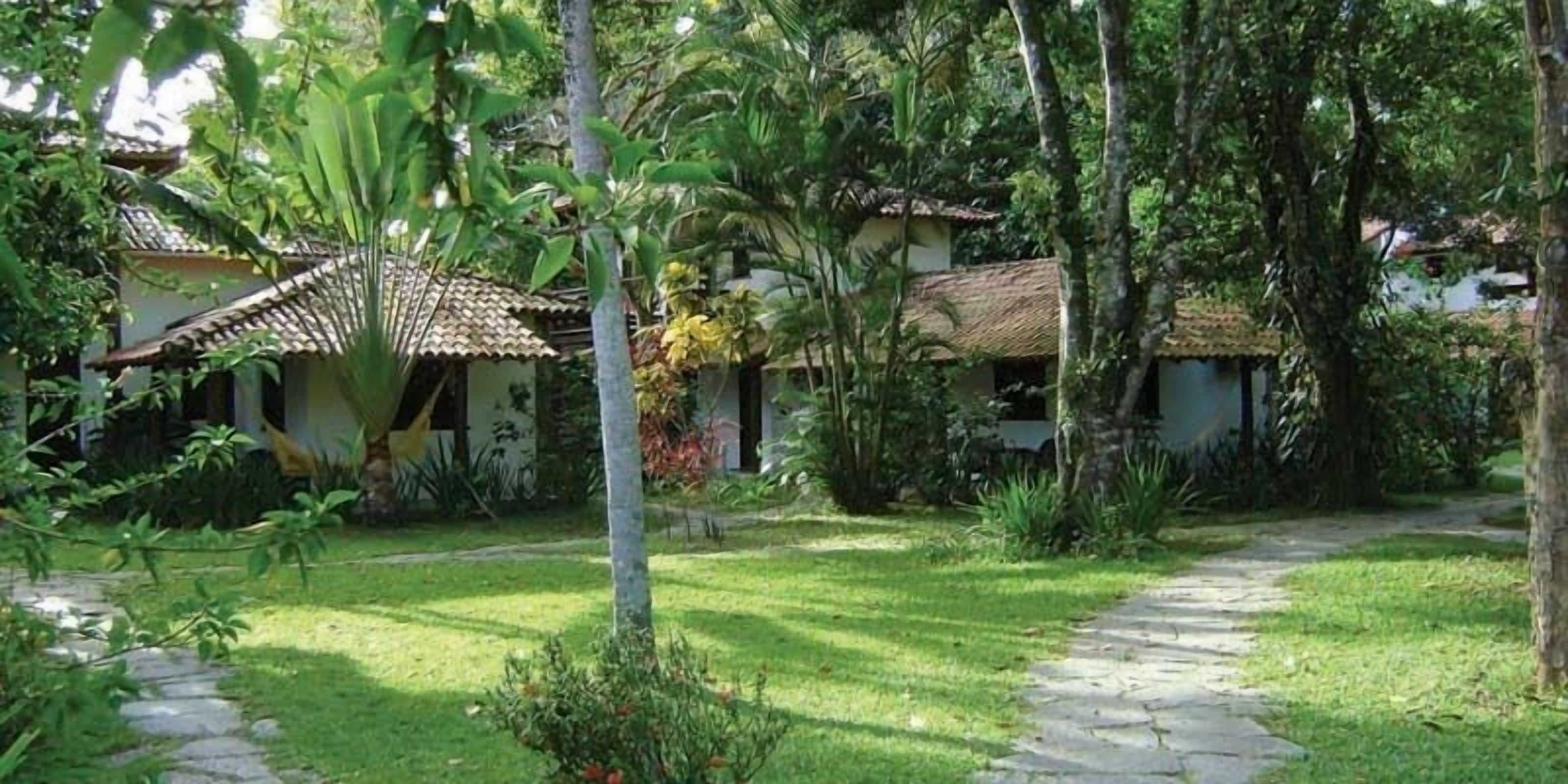 Un sentier de jardin mène à un bâtiment doté d’un toit en tuiles, entouré d’une végétation luxuriante et de plantes tropicales.
