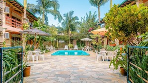 A pool area with stone flooring, white lounge chairs, and umbrellas. - Pousada ChaDay (Imbituba)