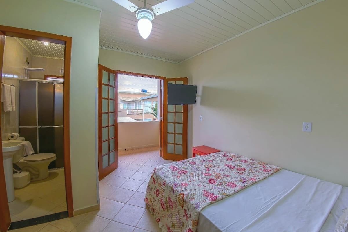 A bedroom with a bed, a television, a bathroom with a toilet and sink, and a balcony.