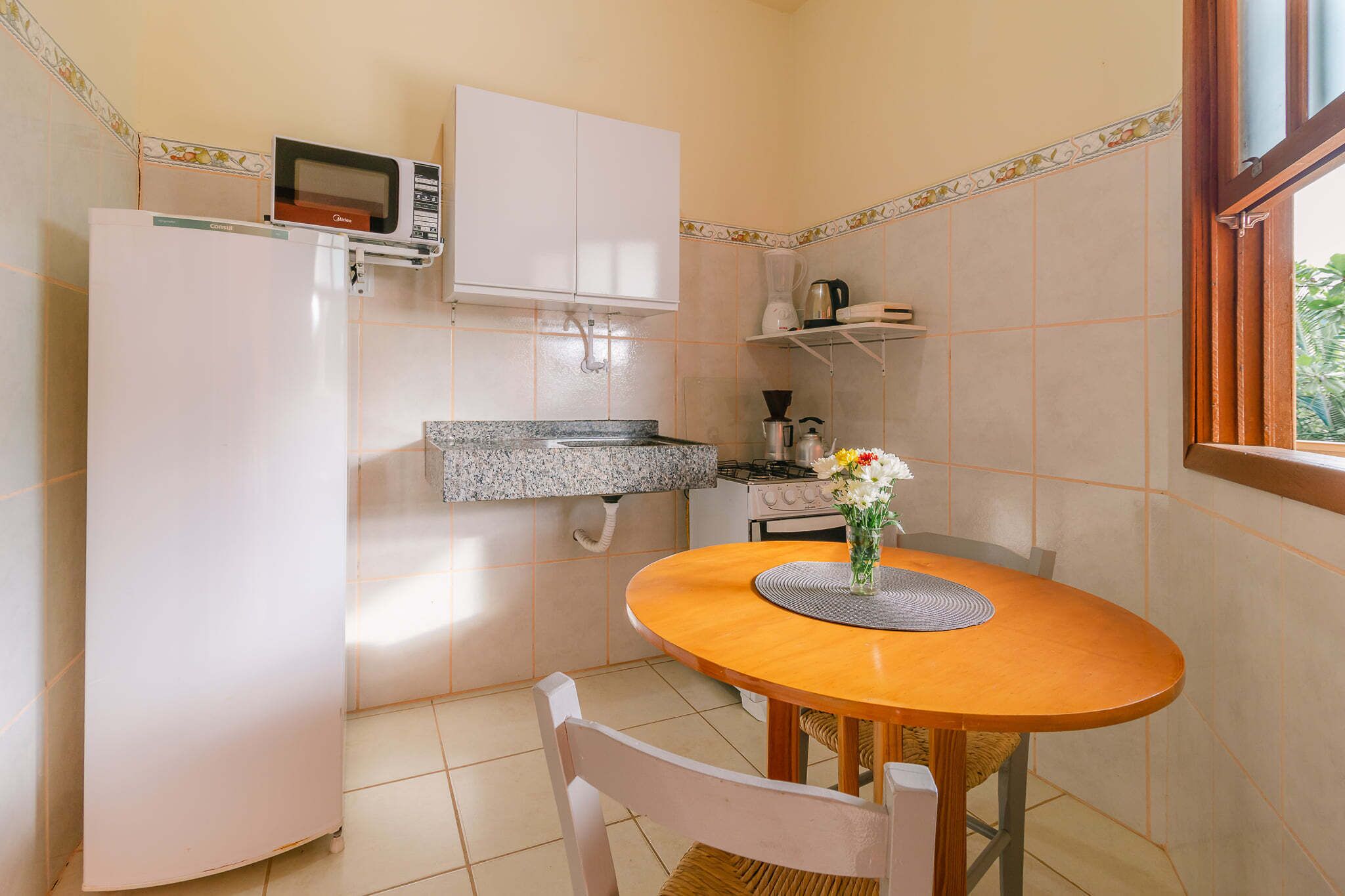 Una cocina compacta equipada con refrigerador, microondas, estufa y una pequeña mesa de comedor con una silla.