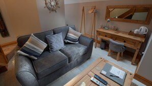 Ein modernes Wohnzimmer mit grauem Sofa, Holzschreibtisch und einem großen Spiegel.