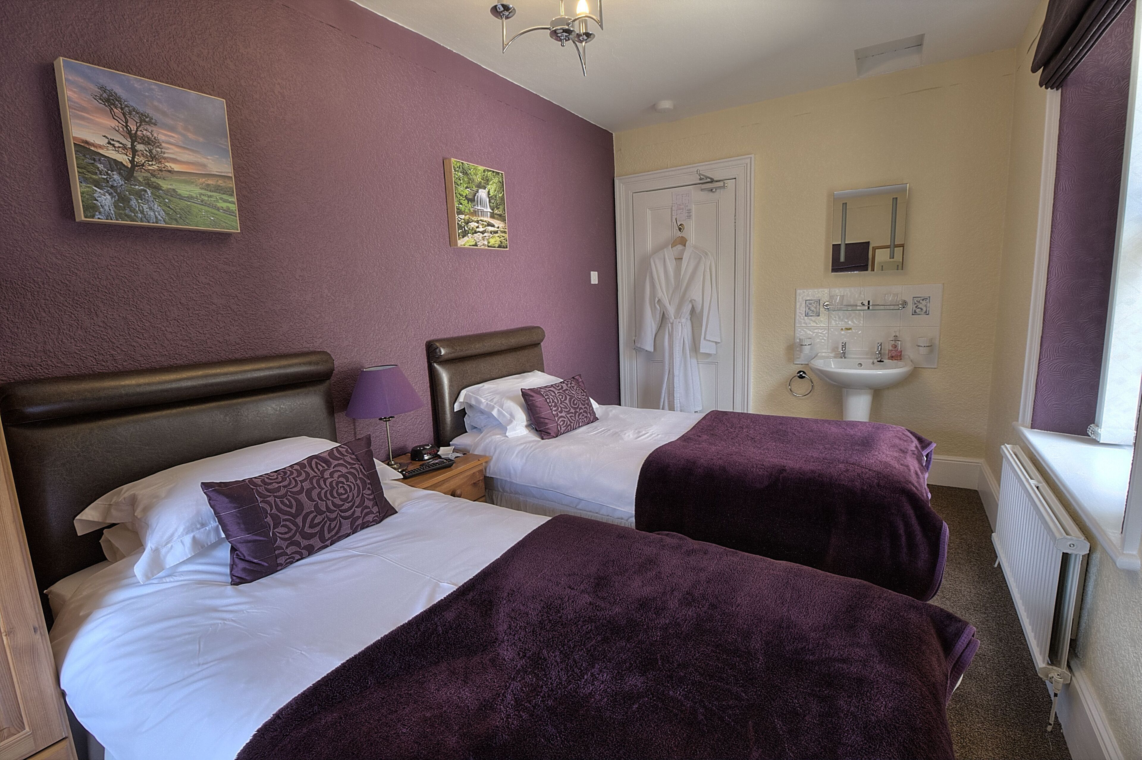 A hotel room with two beds, a bathroom with a sink and mirror, and artwork on the walls.