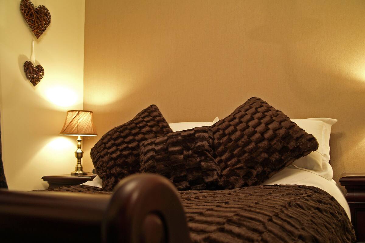 A neatly made bed with a textured blanket and two pillows, a bedside lamp, and two heart-shaped wall decorations.