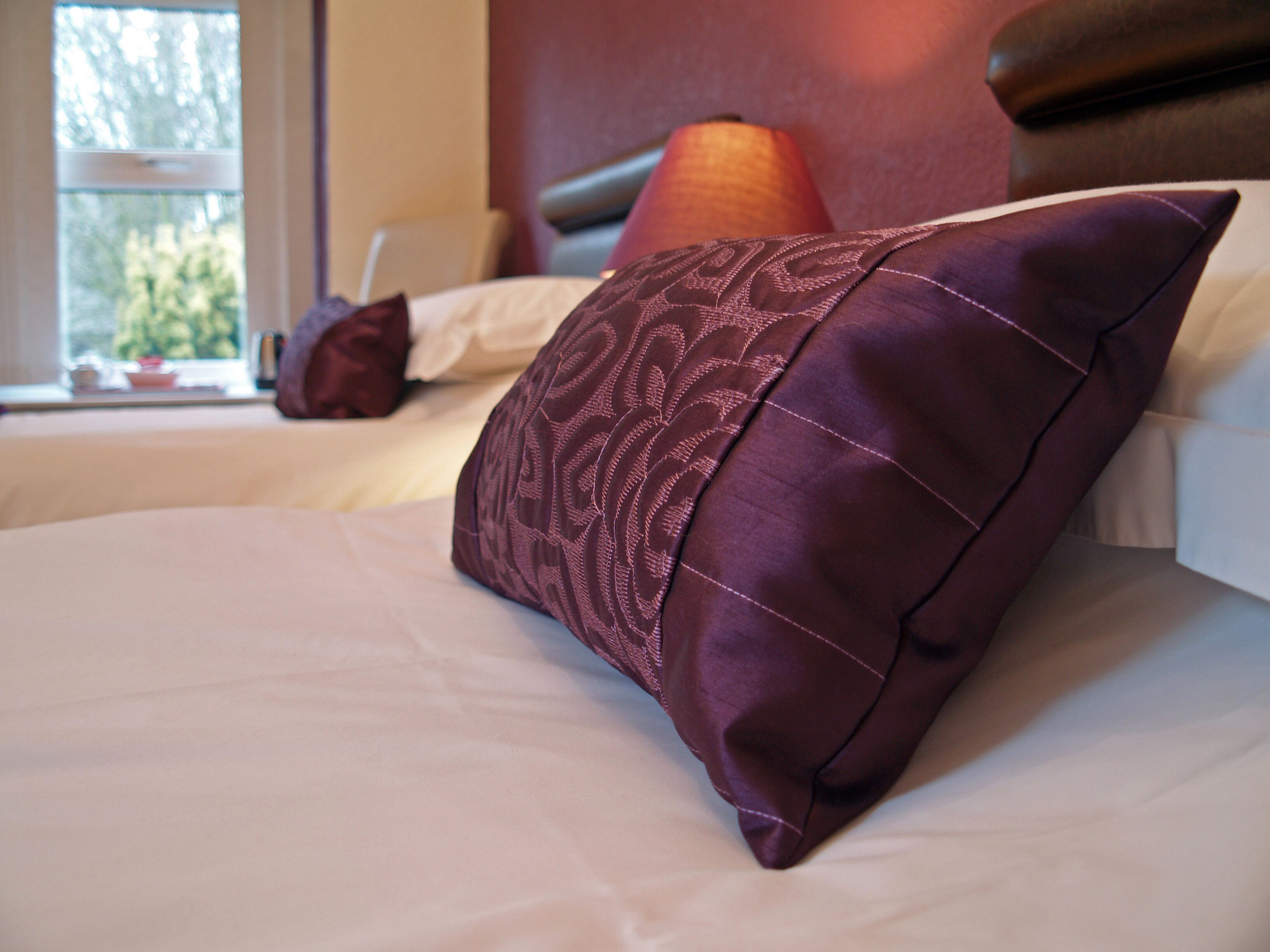 A neatly made bed with a patterned pillow and a plain pillow in a hotel room.