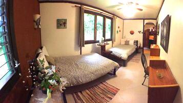 A compact bedroom with a bed, a small table with a vase of flowers, a window, and a door leading to another room.