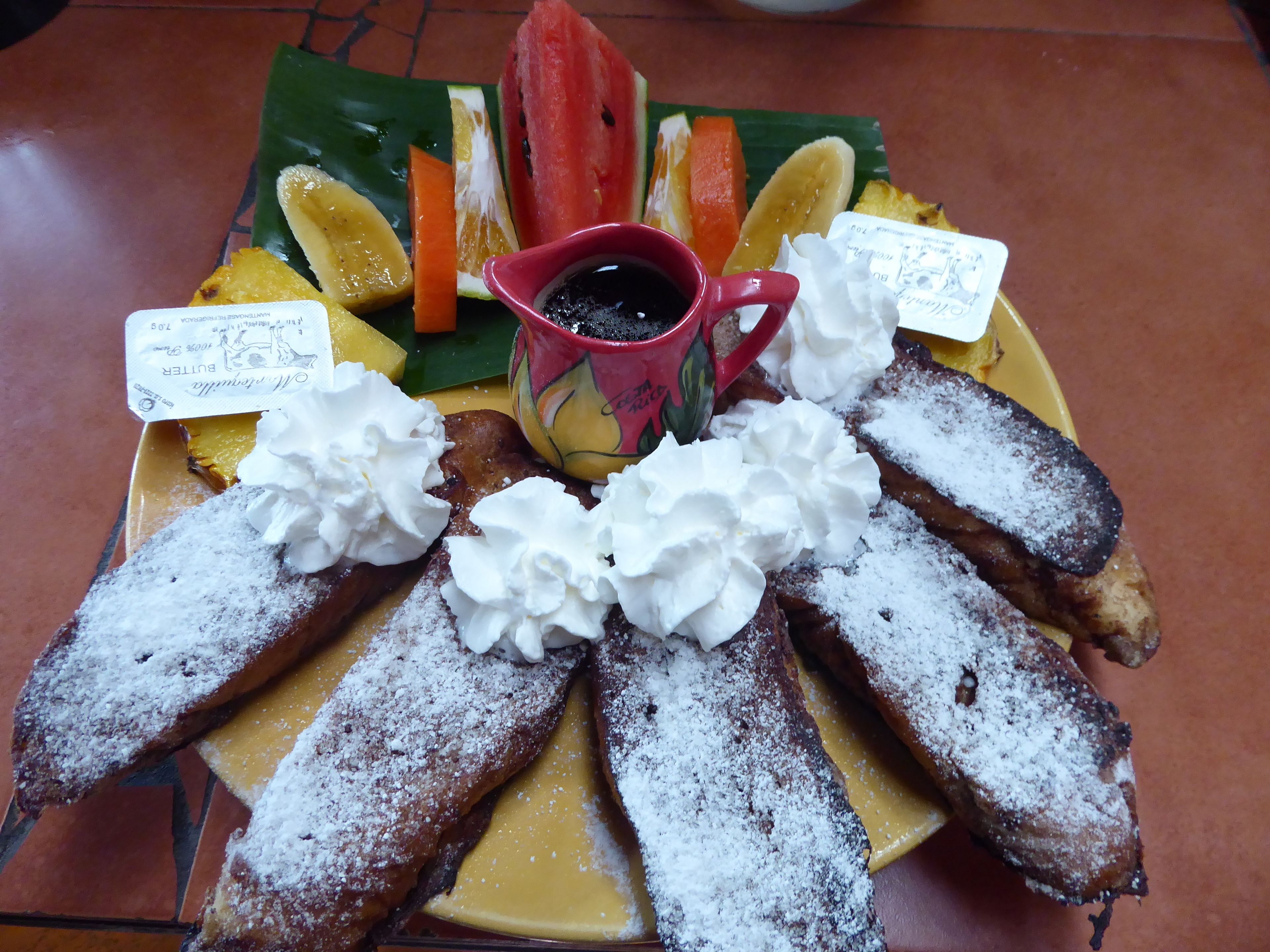 Una bandeja de postres con diversas frutas, crema batida y una taza de café.