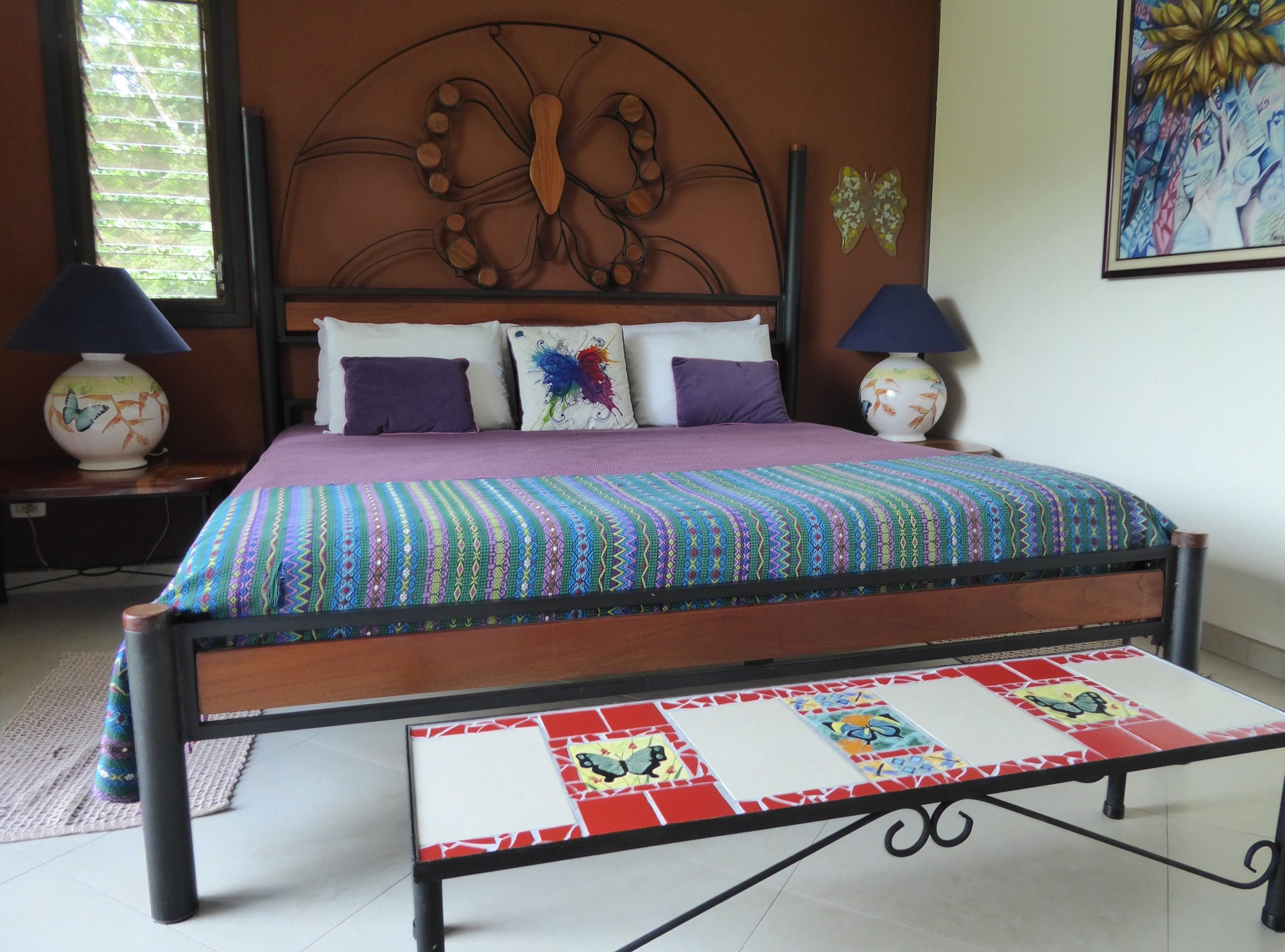 A bed with a colorful quilt, two lamps, and a butterfly wall decoration.