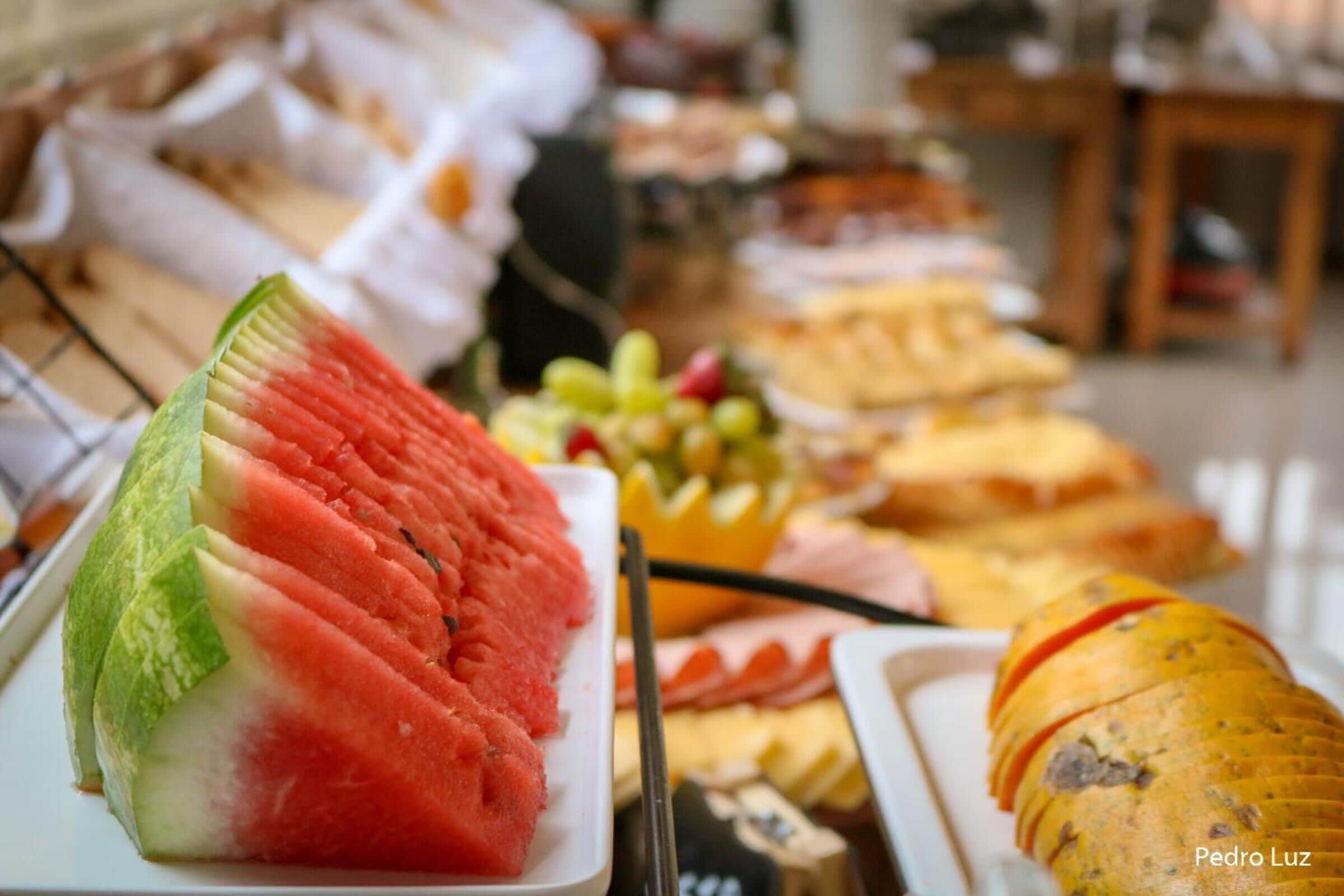 Un buffet proposant une variété d’aliments, notamment des pastèques, des raisins et un pain.