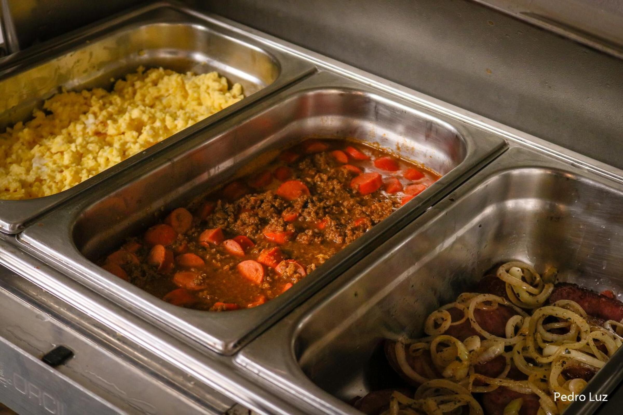 A buffet with various dishes including scrambled eggs, a meat dish with carrots, and a steak topped with onions.