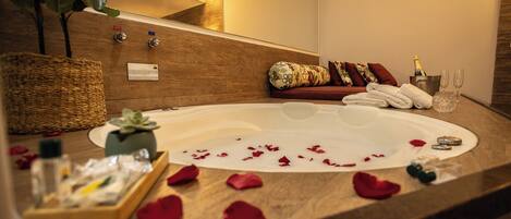 Un cuarto de spa con un jacuzzi, un banco de madera, una botella de champán y una cesta.