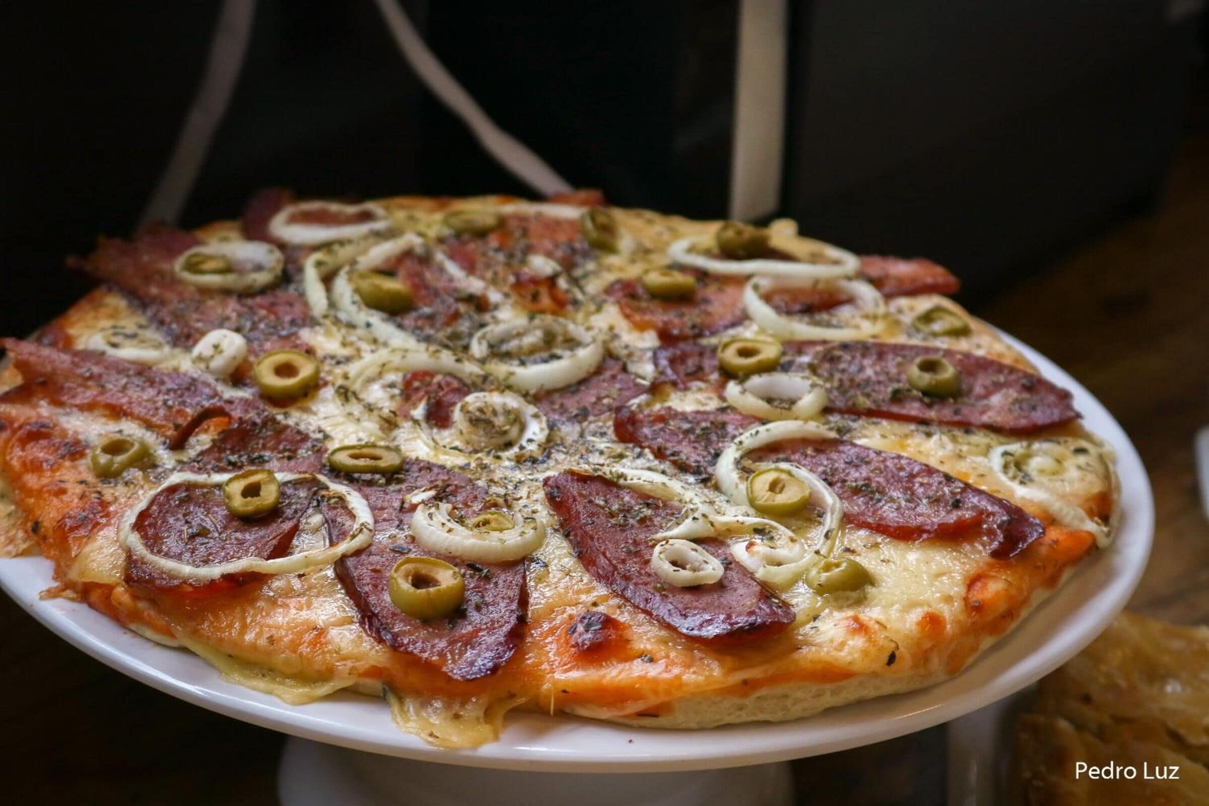 Une pizza garnie de pepperoni, d’olives et d’oignons, servie sur une assiette blanche.