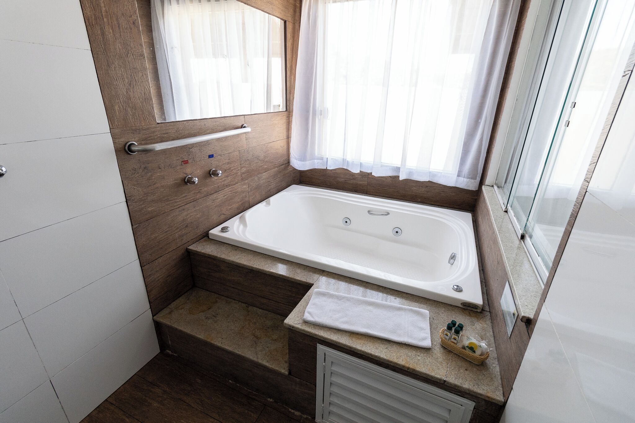 A modern bathroom with a bathtub, a shower, a vanity with a mirror, and a window with curtains.