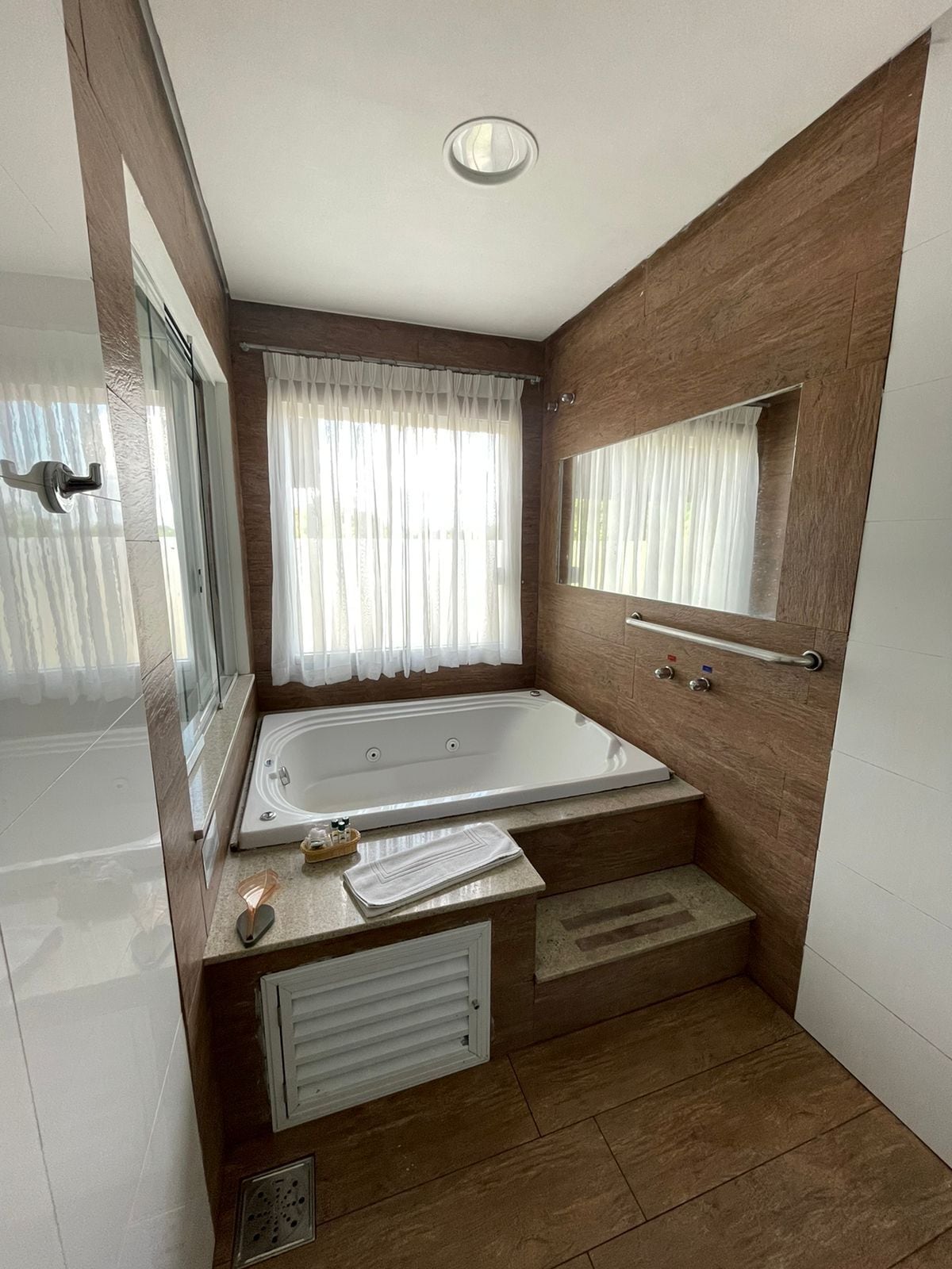 A modern bathroom with a bathtub, a window with curtains, a mirror, and a towel rack.