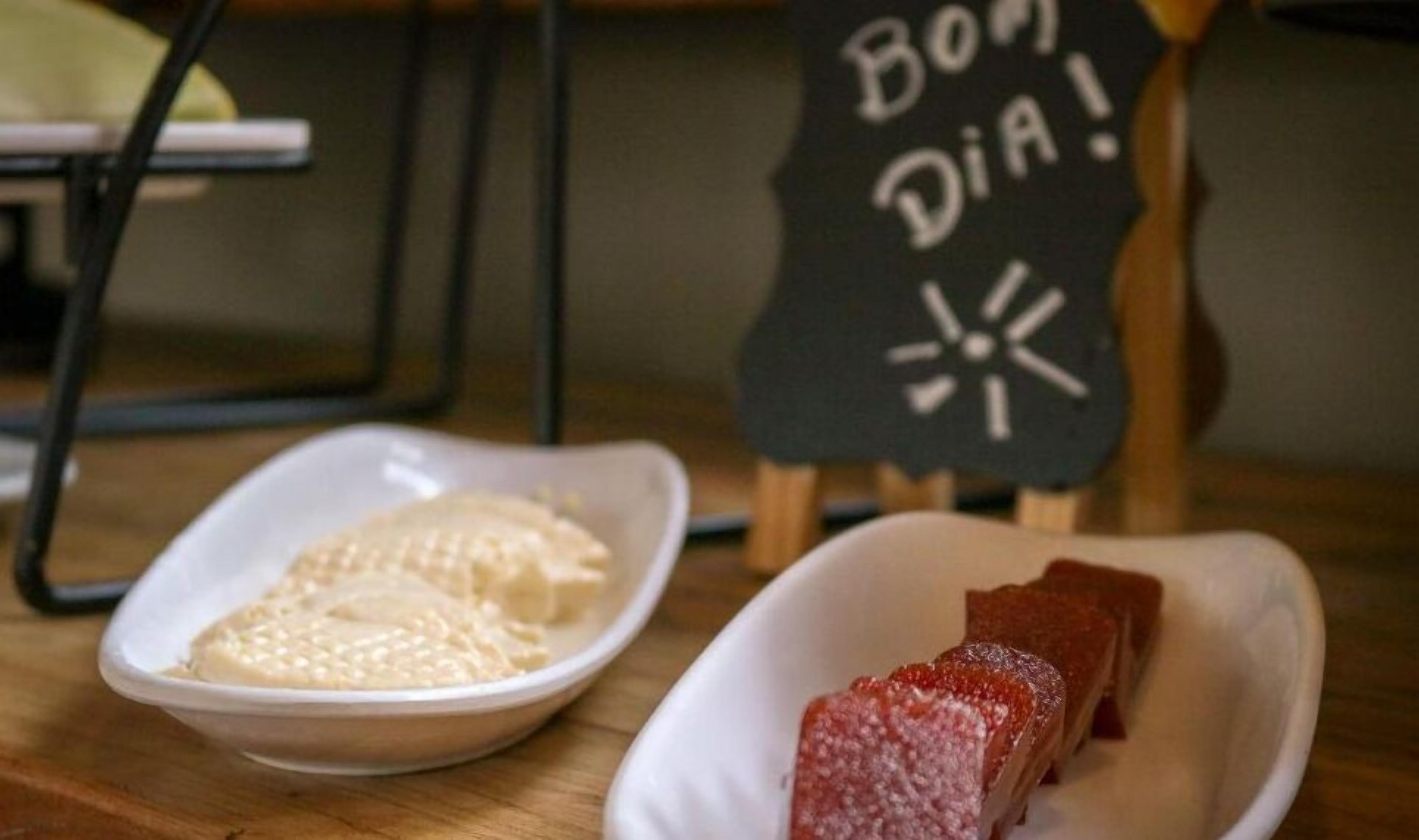 A table with two white dishes, one containing a white food item and the other a red food item, with a sign reading "Bom Dia!" in the background.