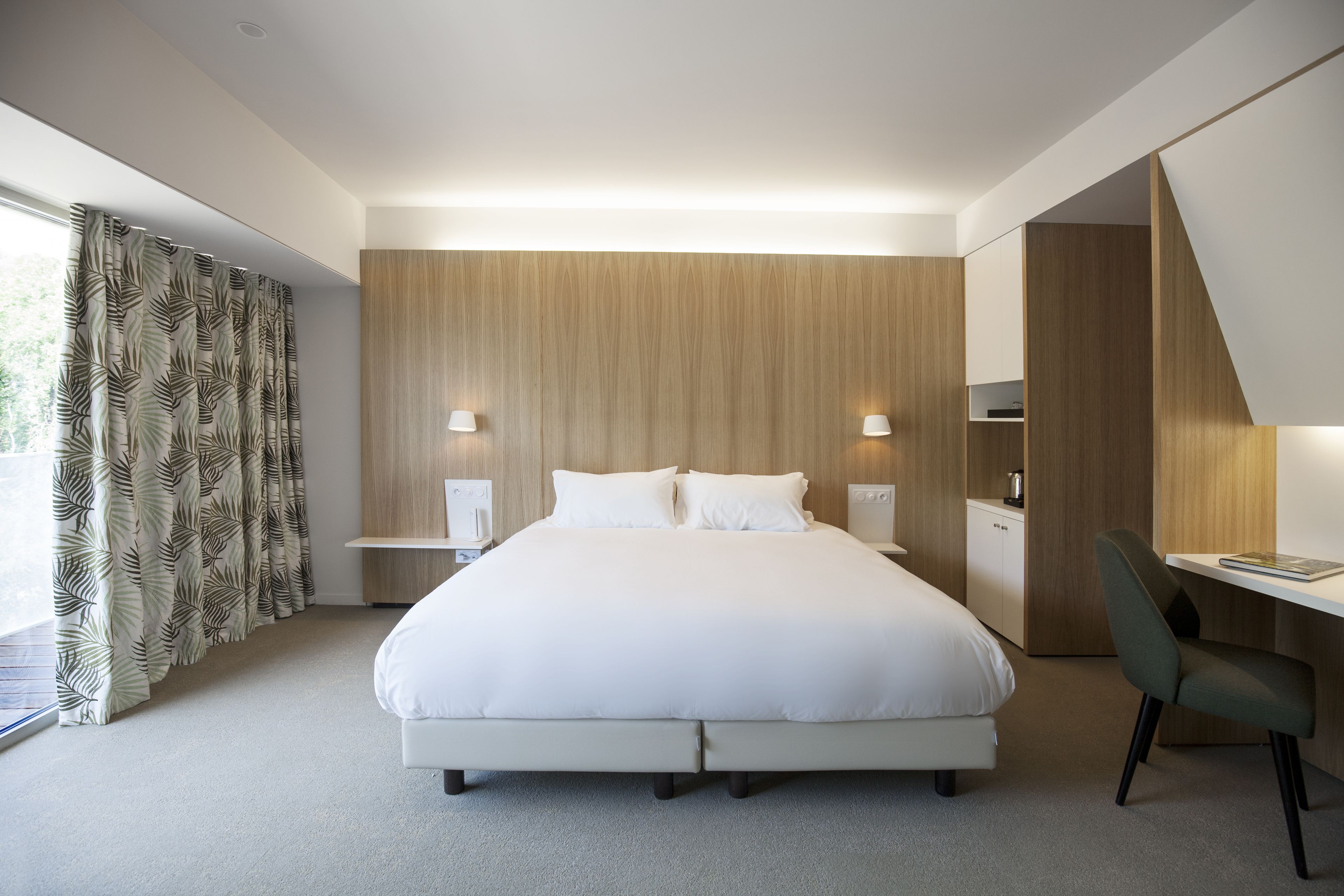 Una habitación de hotel moderna con una cama grande, lámparas de noche, un escritorio y una silla.