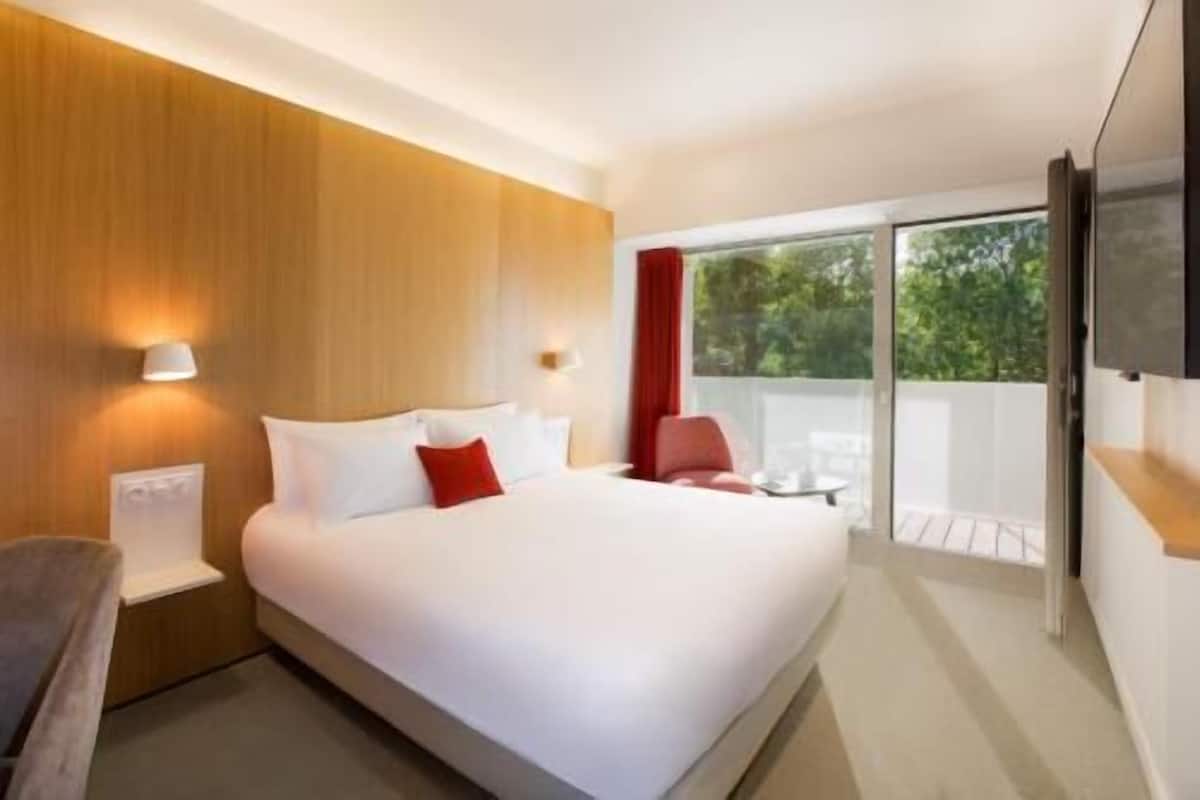 Une chambre d’hôtel moderne dotée d’un grand lit, d’une télévision à écran plat, d’un balcon avec une table et des chaises, et d’un mur en bois.
