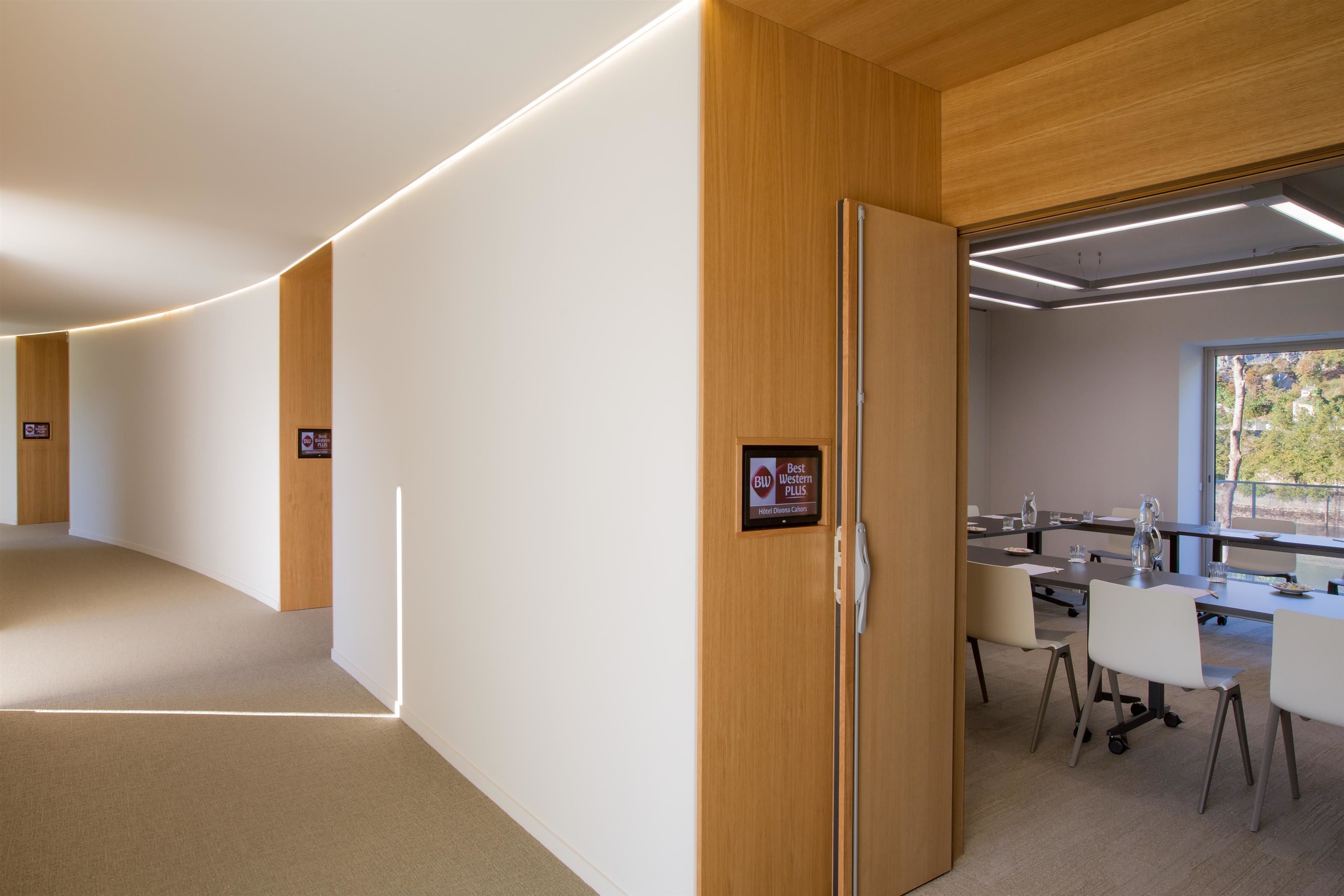 A modern hotel lobby with a curved wall, a reception desk, and a conference room with tables and chairs.