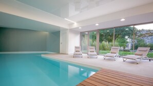 A modern indoor swimming pool with clear glass walls, wooden deck, and lounge chairs. - Best Western Plus Hotel Divona Cahors (Cahors)