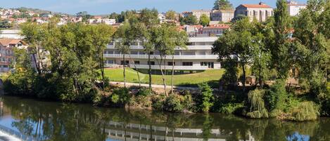 A riverside view with a building complex, trees, and a clear sky.