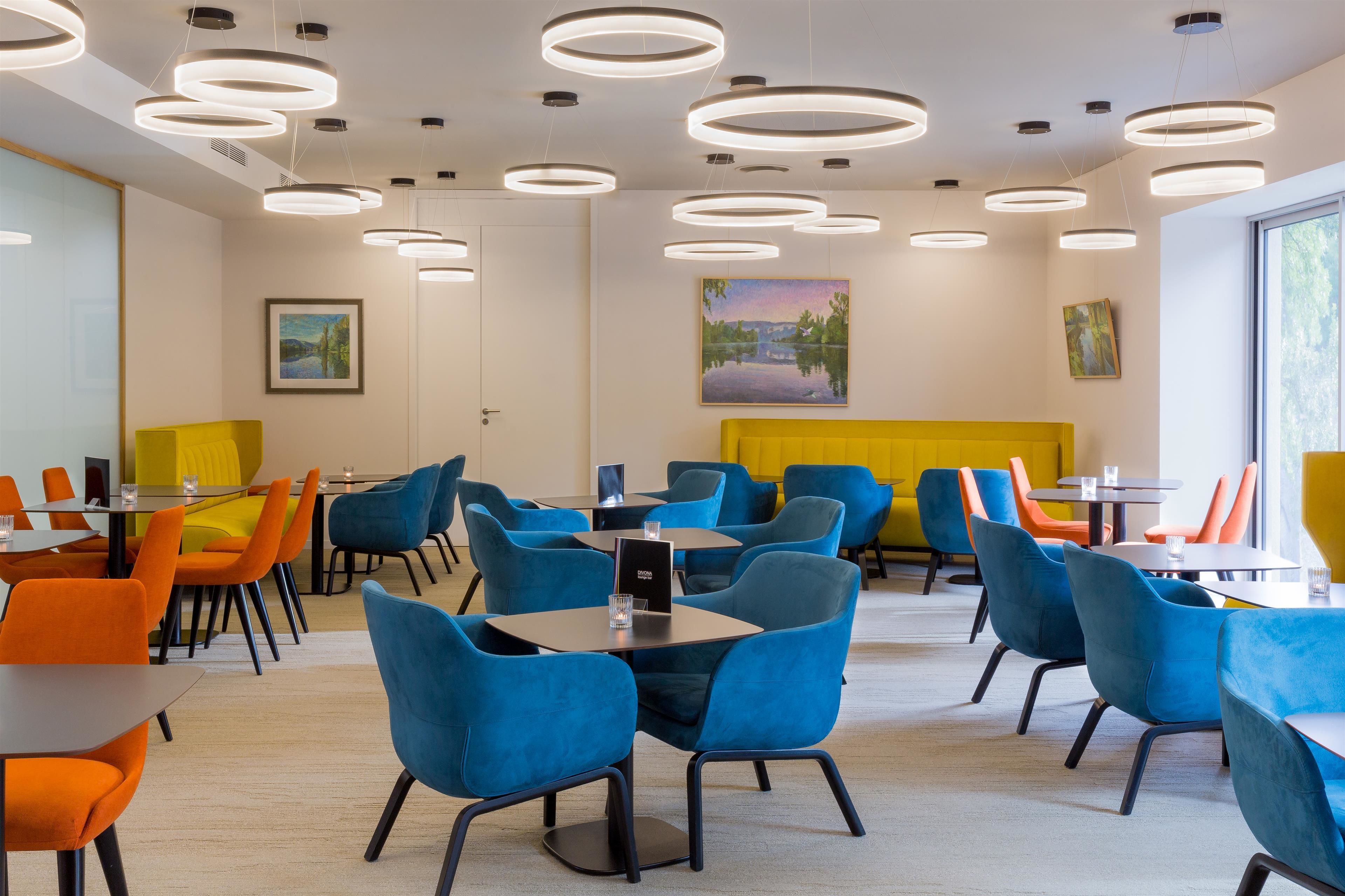 A modern dining area with round tables and chairs, a yellow accent wall, and artwork on the walls.