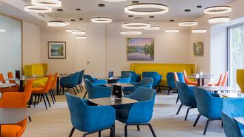 Un espace de restauration moderne avec des tables et des chaises rondes, un mur d’accent jaune et des œuvres d’art accrochées aux murs.