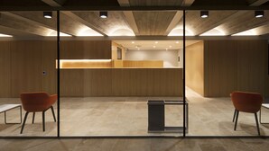 Ein modernes Interieur mit einer Rezeption, zwei orangefarbenen Sesseln und einer Glastrennwand.