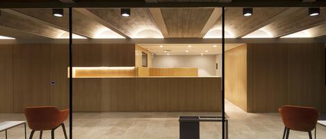 A modern interior with a reception desk, two orange chairs, and a glass partition.