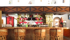 Zona de bar con taburetes de mimbre, pared de piedra y varios botellas y vasos en estantes.