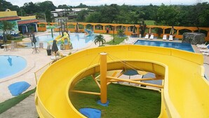 Un parque acuático con un tobogán amarillo grande, varias piscinas y zonas de descanso con sombrillas.