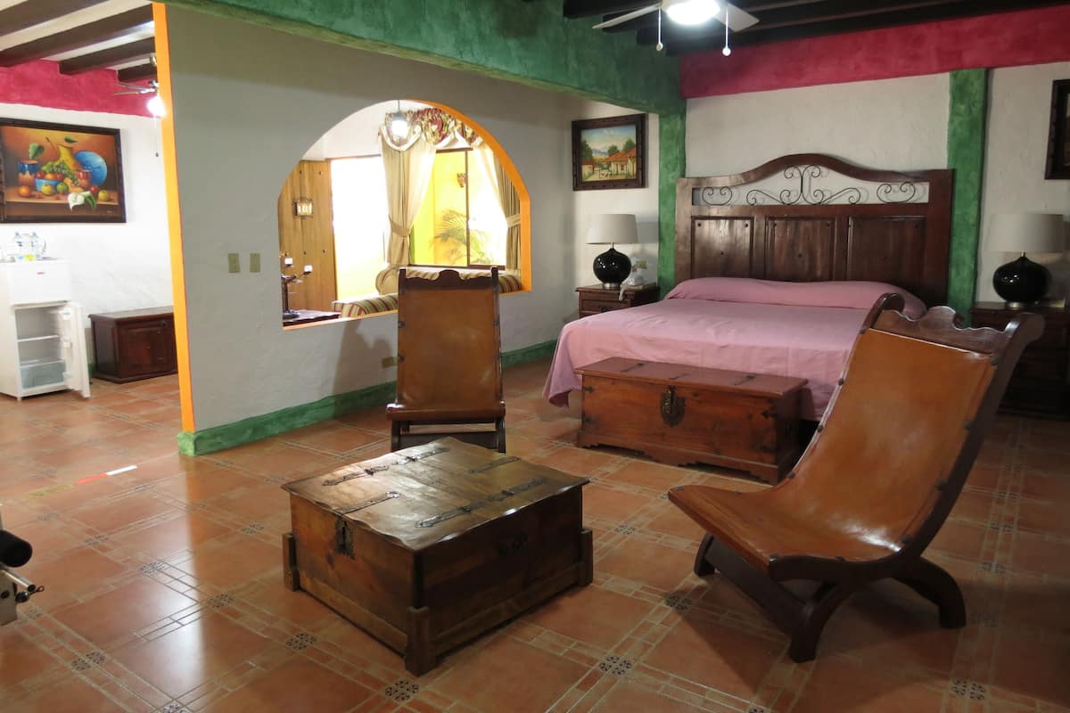A bedroom with a bed, a wooden chest, a chair, a nightstand, and a mirror.