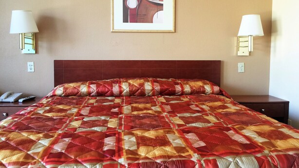 A hotel room with a large bed, two bedside lamps, a framed picture on the wall, and a phone on the nightstand. - Bama Inn (Huntsville)