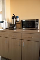 A kitchenette with a coffee maker, microwave, and cabinets.