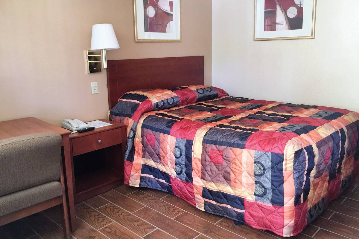 A hotel room with a bed, a desk, a lamp, and two framed pictures on the wall.