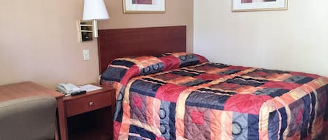 Habitación de hotel con cama, escritorio, lámpara y dos cuadros en la pared.