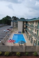 A hotel with a swimming pool, outdoor seating, and a parking lot.