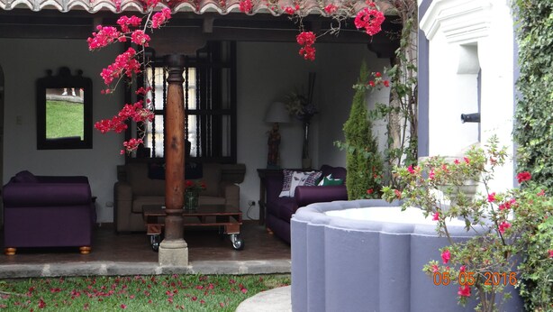 A covered outdoor seating area with a table and chairs, surrounded by lush greenery and flowering plants. - Hotel Casa Naranjo (Antigua Guatemala)