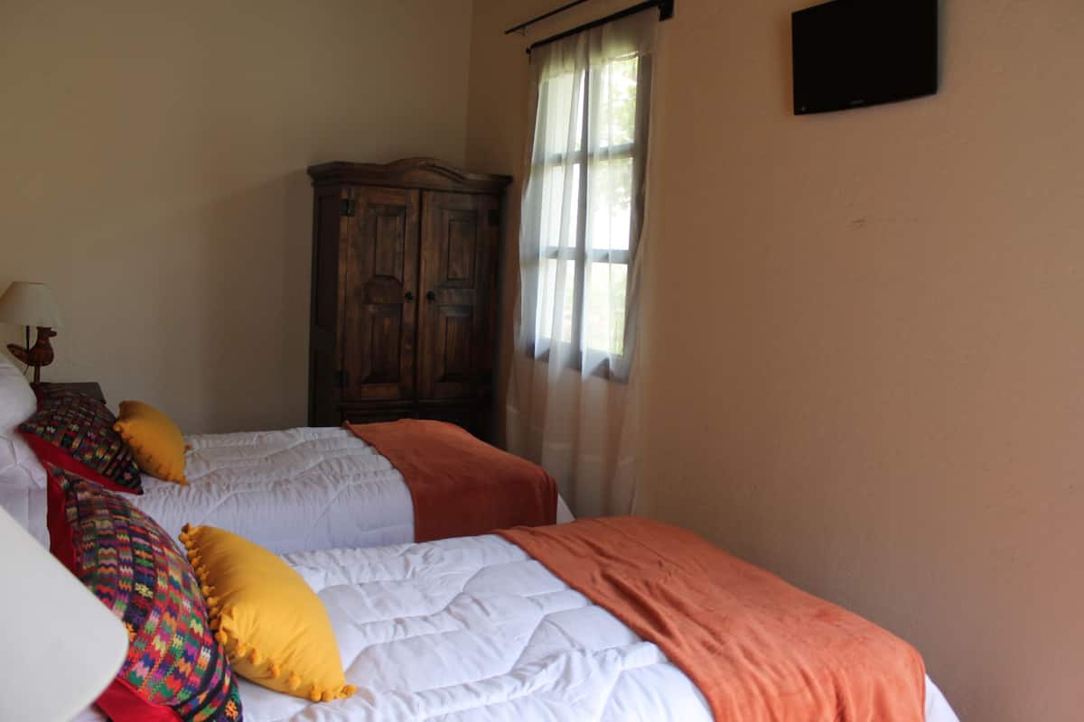 Un dormitorio con dos camas, un armario de madera y una ventana con cortinas.
