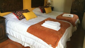 A hotel room with two beds, each with white bedding and orange throw blankets. There are colorful pillows on the beds, and a lamp on a nightstand. - Hotel Casa Naranjo (Antigua Guatemala)