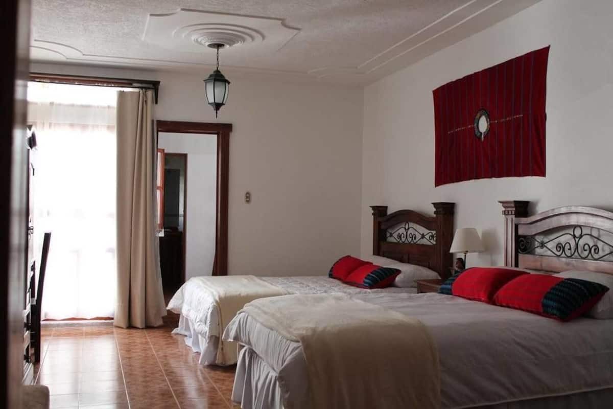Een hotelkamer met twee bedden, een rode vlag aan de muur, een houten hoofdeinde en een plafondlamp.