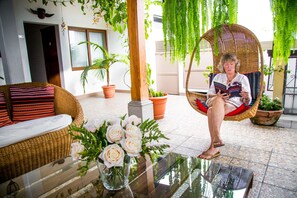 Ein Korbusofa mit roten und schwarzen Kissen, ein Glastisch mit einer Rosenvase und ein Korbschaukelstuhl mit einer Person, die ein Buch liest.