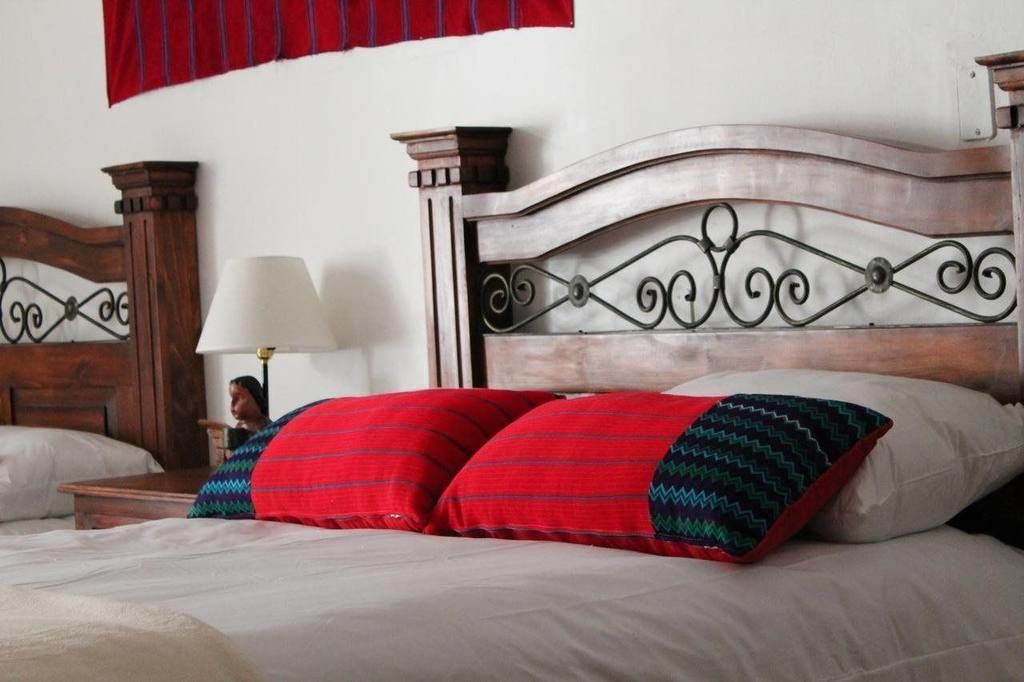 A neatly made bed with a wooden headboard and decorative metalwork, accompanied by a nightstand with a lamp.