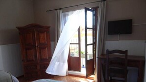 Een slaapkamer met een bed, een houten garderobe, een bureau met stoel en een televisie aan de muur.